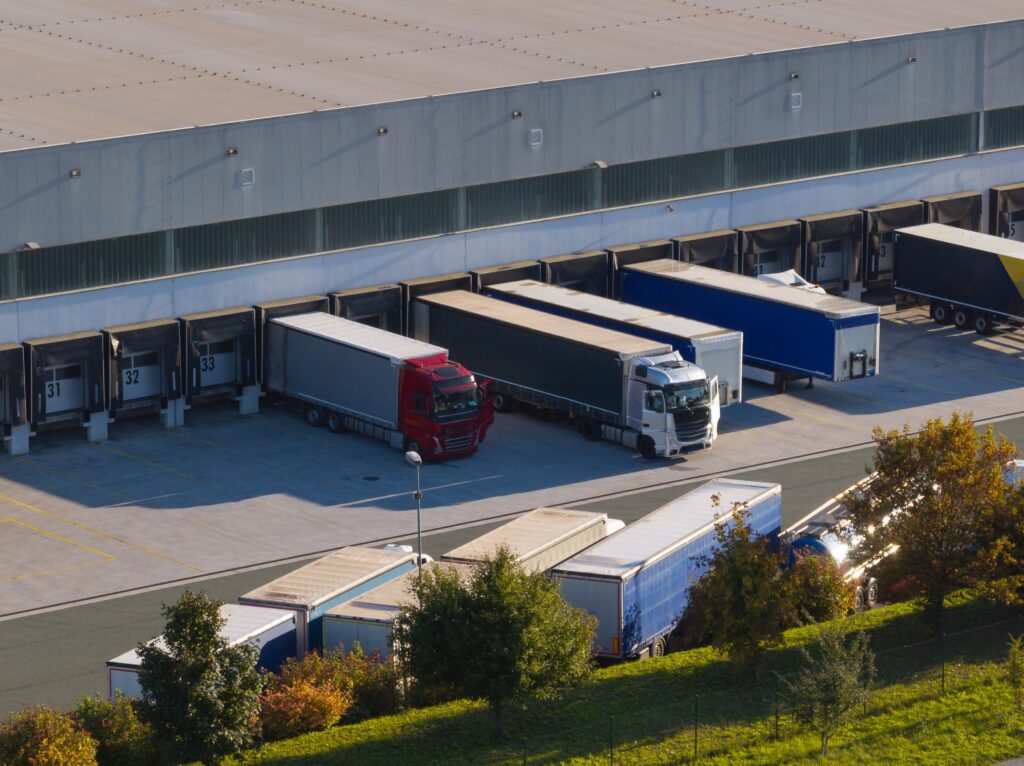 Semi-trucks and trailers lined up at warehouse loading docks for freight pickup and delivery.
